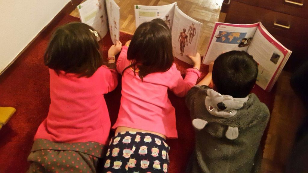 3 refugee children happily read their new schoolbooks from MFR donors